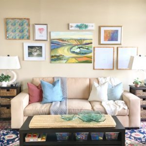 The interior design of this bright and cheerful family room showcases a colorful gallery wall behind the cream colored couch.