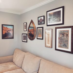 The modern interior design of this room showcases a gallery wall with several framed art pieces of varying sizes and a teardrop shaped mirror.