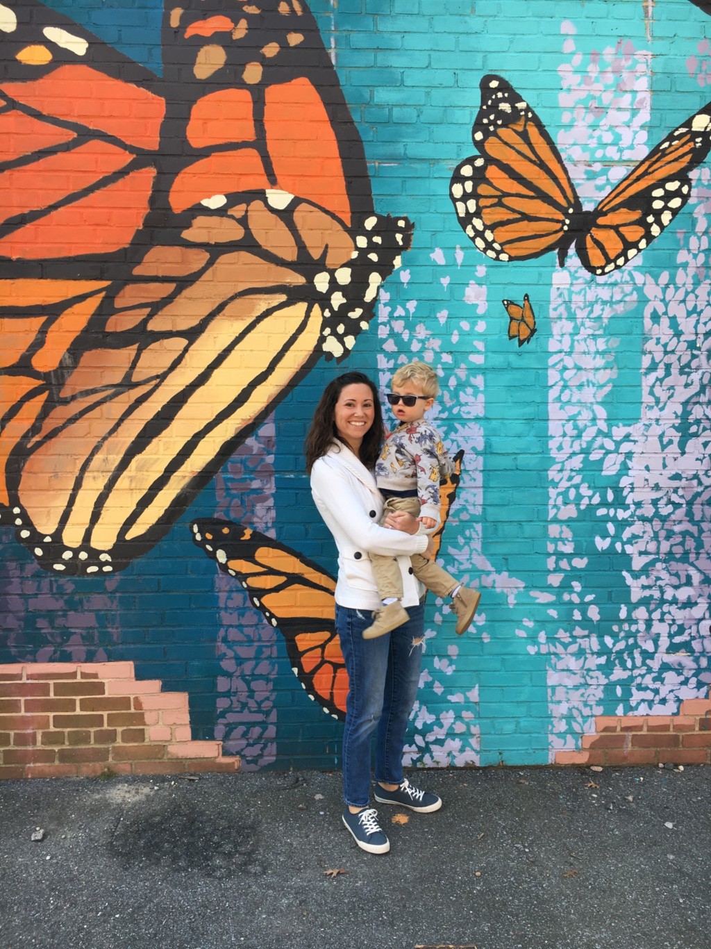 A mother holds her toddler son in front of a gorgeous wall mural painted with oversized monarch butterflies.