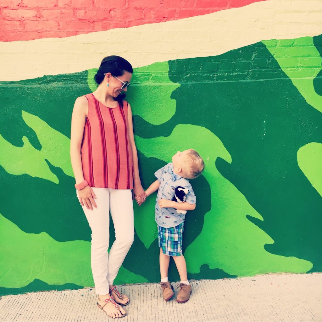 A mother and young son hold hands in front of the Watermelon House mural in Washington DC.