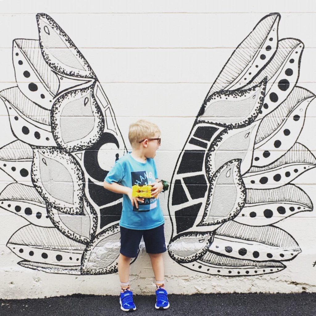 A young boy looks back over his shoulder in surprise at the mural of a pair of wings painted on the wall behind him.