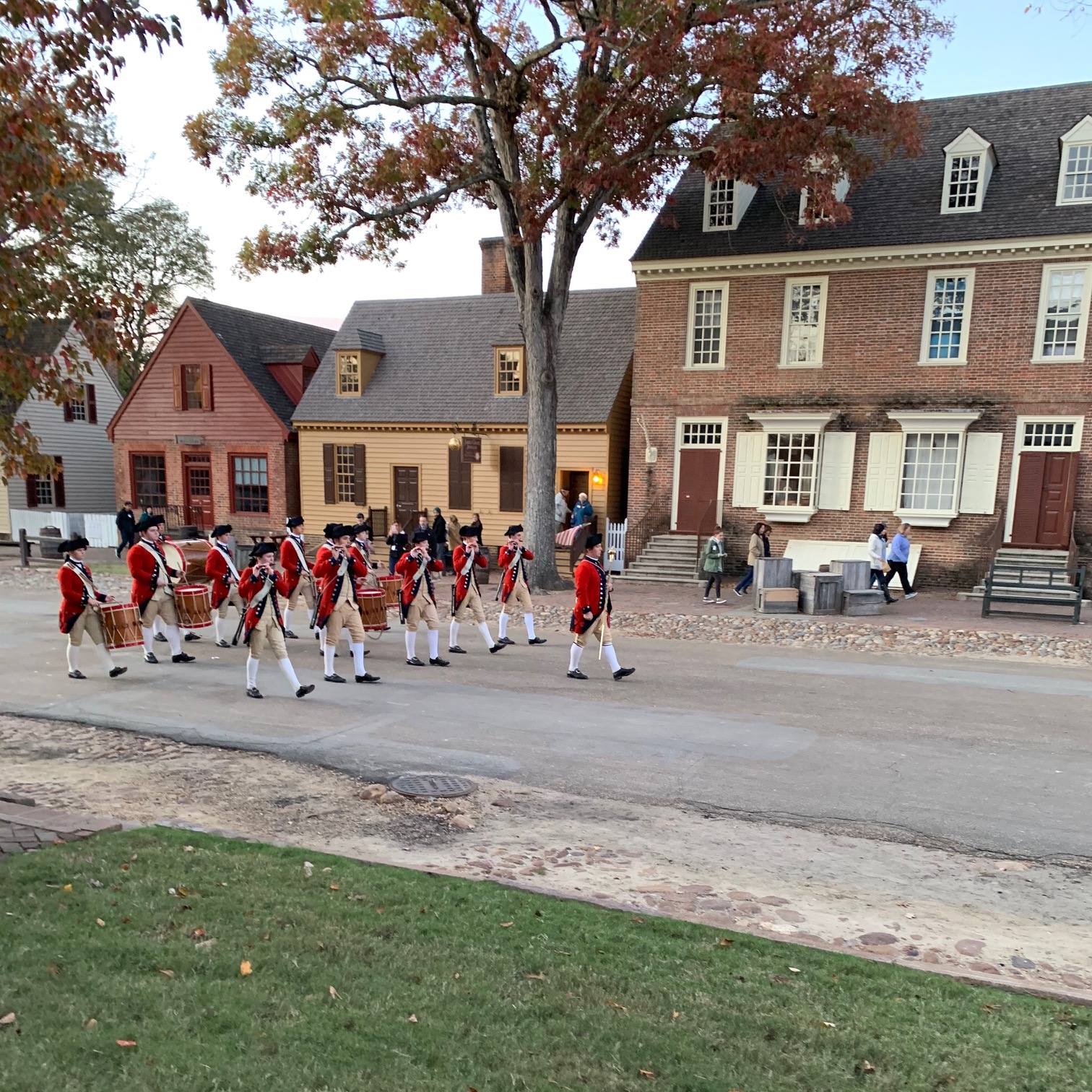 The Colonial Williamsburg Fifes and Drums march down the street wearing the distinctive red coats of British military uniforms.