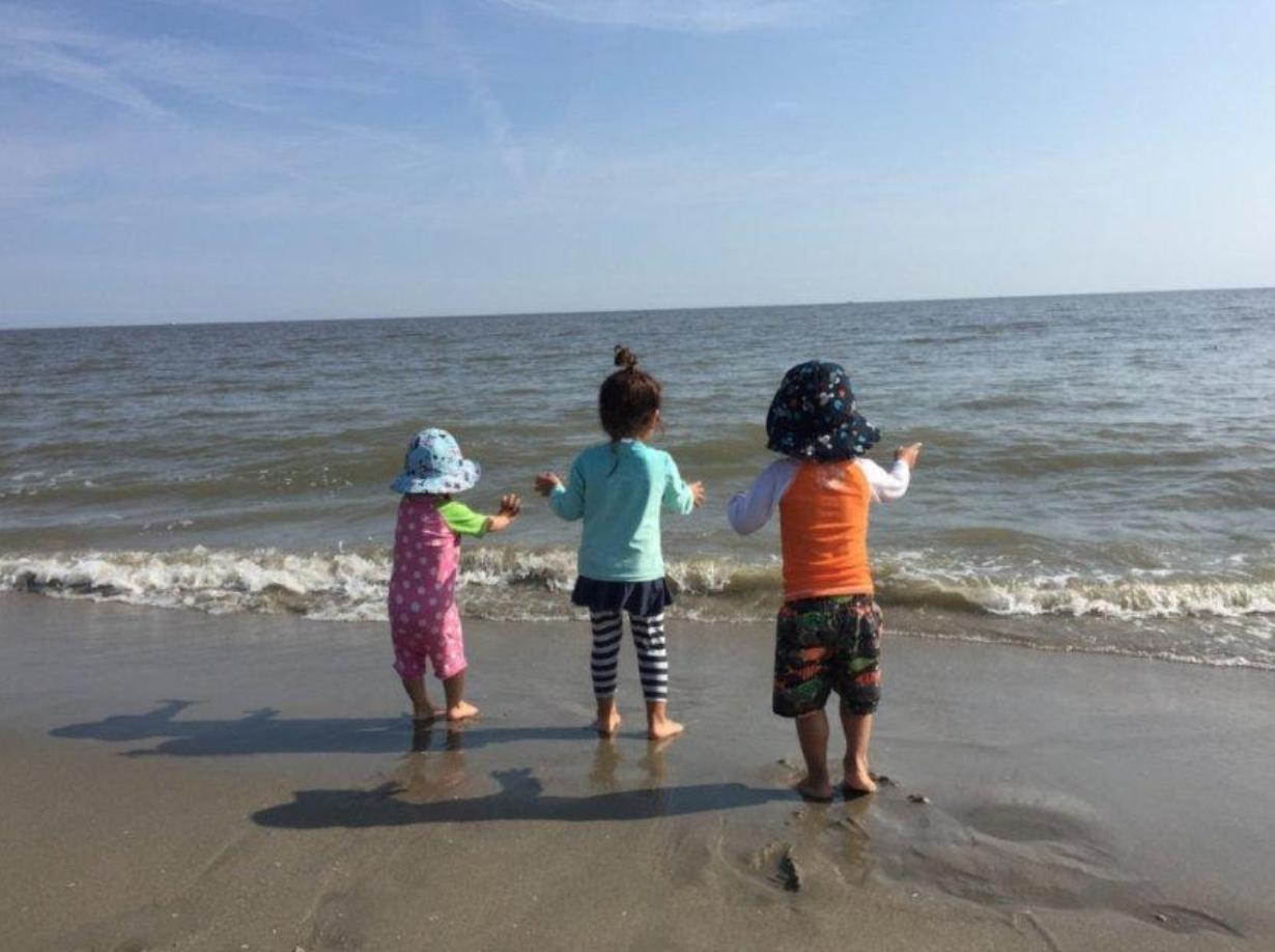 Three children look out at the ocean together.