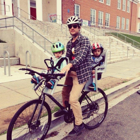 A father bikes with two children, which is a sustainable way to saving planet earth.