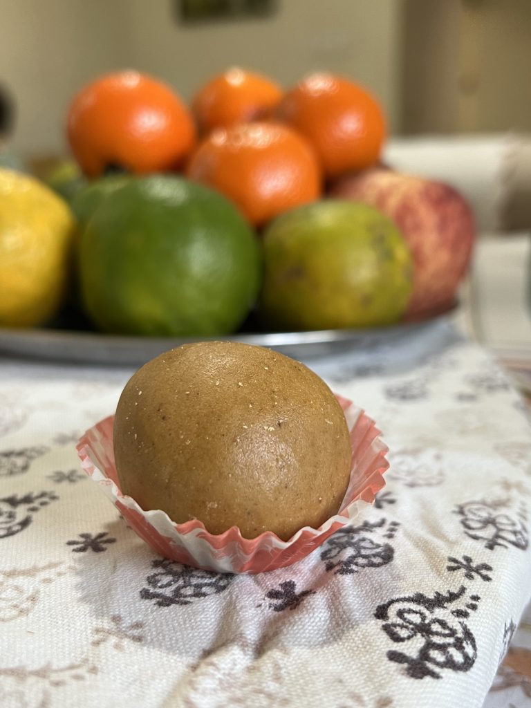 a besan laddoo in front of a plate of fruit