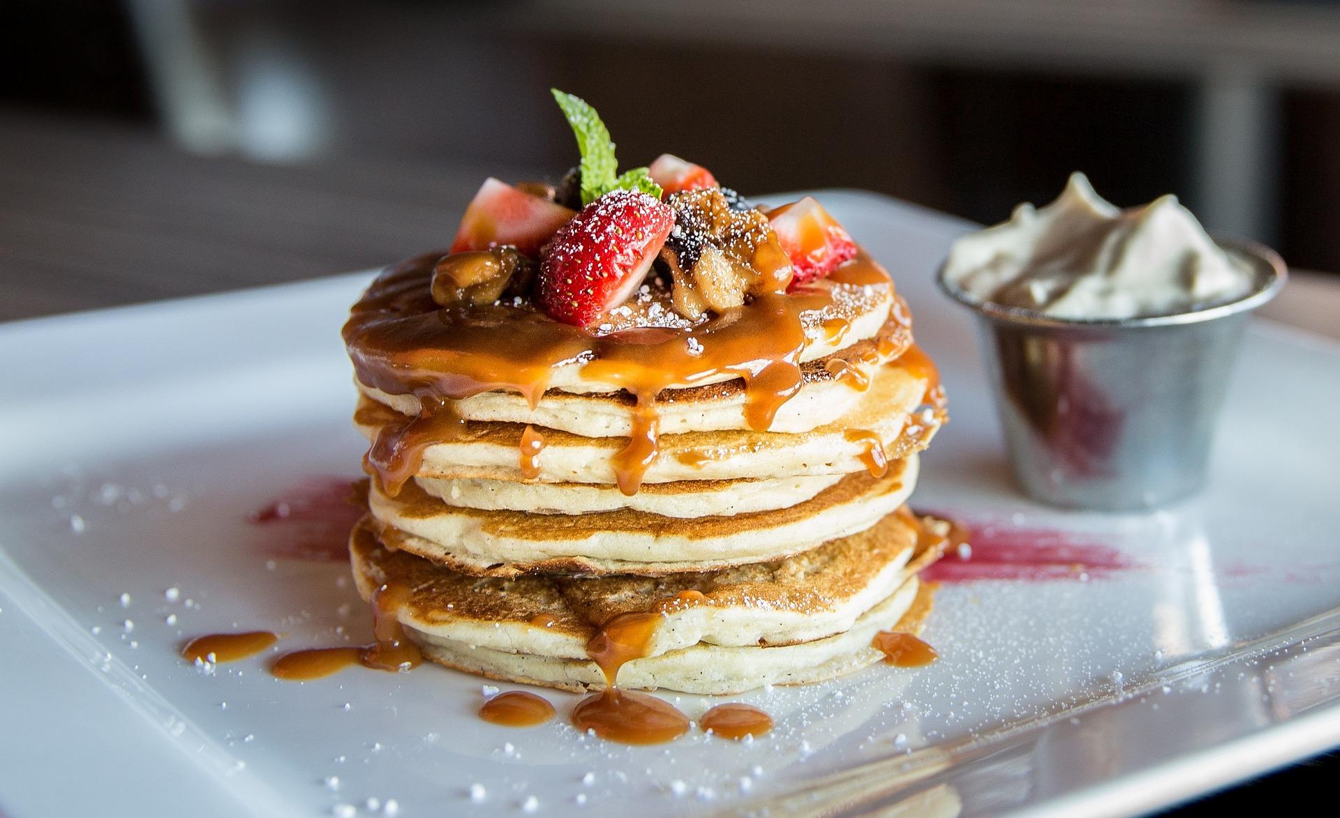 A stack of pancakes with fruit and whipped cream.