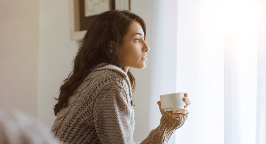 Woman looking out window holding cup. I don't like Mother's Day