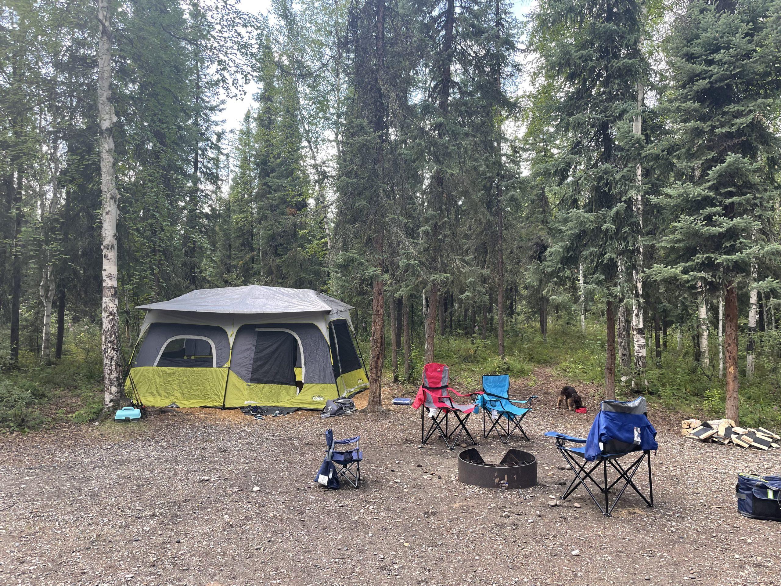 A tent and camp chairs are in a forest.