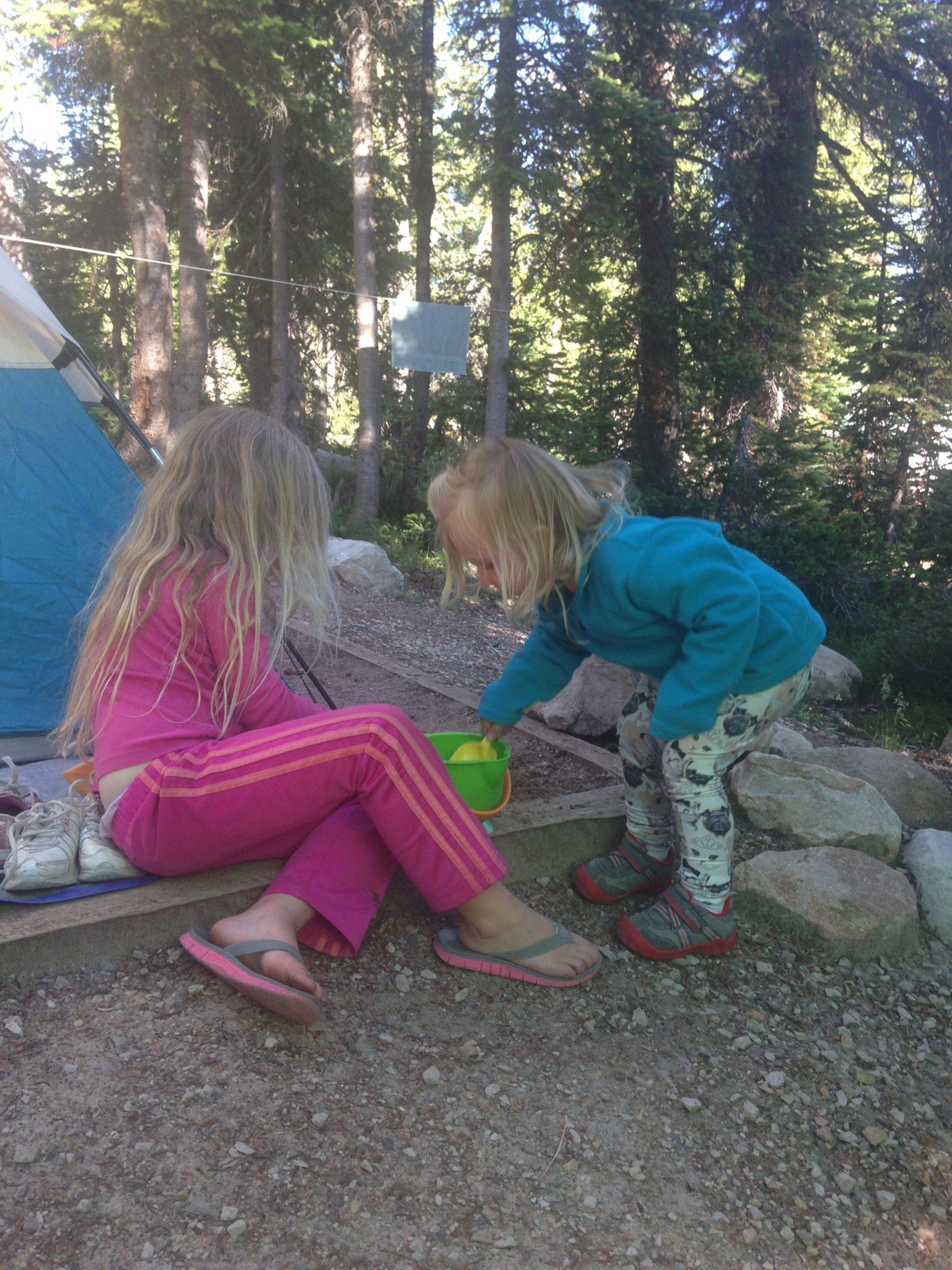 Two girls digging in the dirt while camping in a forest. 