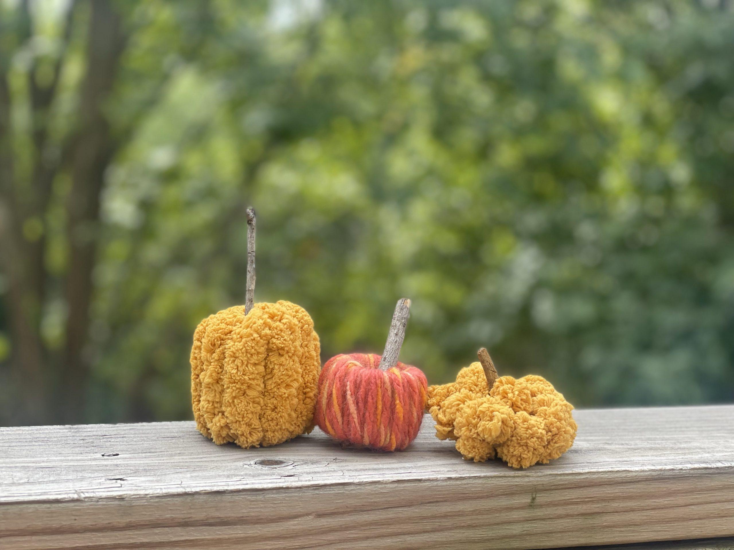 3 small pumpkins made of yarn are sitting on a wooden ledge. 
