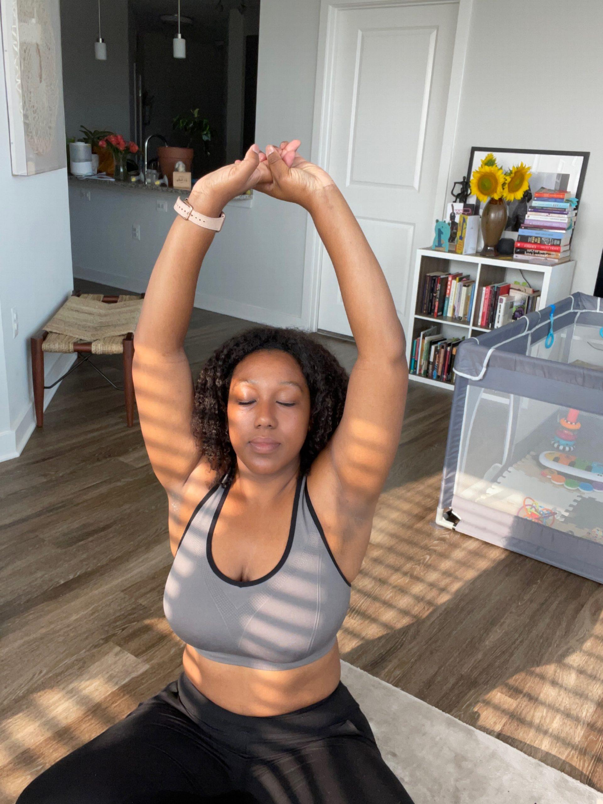 A Black woman in the middle of her living room doing a yoga pose with her eyes closed. 