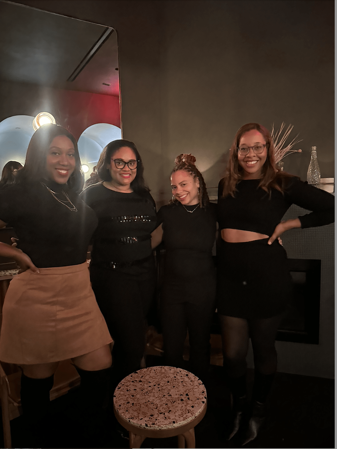Four black women pose for a photo in a dimly lit restaurant